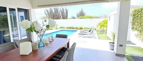 A modern outdoor dining area with a pool, lounge chairs, and a view of the ocean.