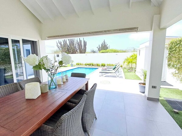 A modern outdoor dining area with a pool, lounge chairs, and a view of the ocean.