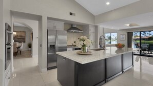 Een moderne keuken met een groot eiland, roestvrijstalen apparatuur en uitzicht op het buitenleven.