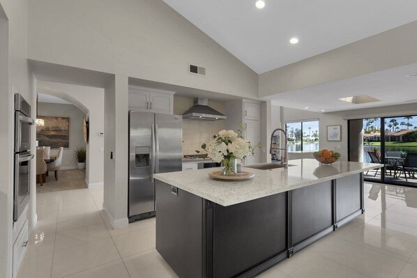 A modern kitchen with a large island, stainless steel appliances, and a view to the outdoors. - PGA West retreat with private pool, spa, and golf views. (La Quinta)