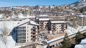 Un hotel de varios pisos con balcones, un estacionamiento y vistas de edificios y colinas circundantes.
