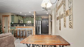 Una cocina con armarios verdes, un refrigerador de acero inoxidable y una mesa de comedor de madera con taburetes.