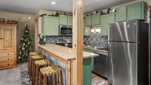 Una cocina con armarios verdes, un refrigerador de acero inoxidable, un microondas e isla de madera con taburetes.