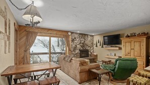Una sala de estar acogedora con chimenea de piedra, televisor montado en la pared y una mesa de comedor de madera con bancos.