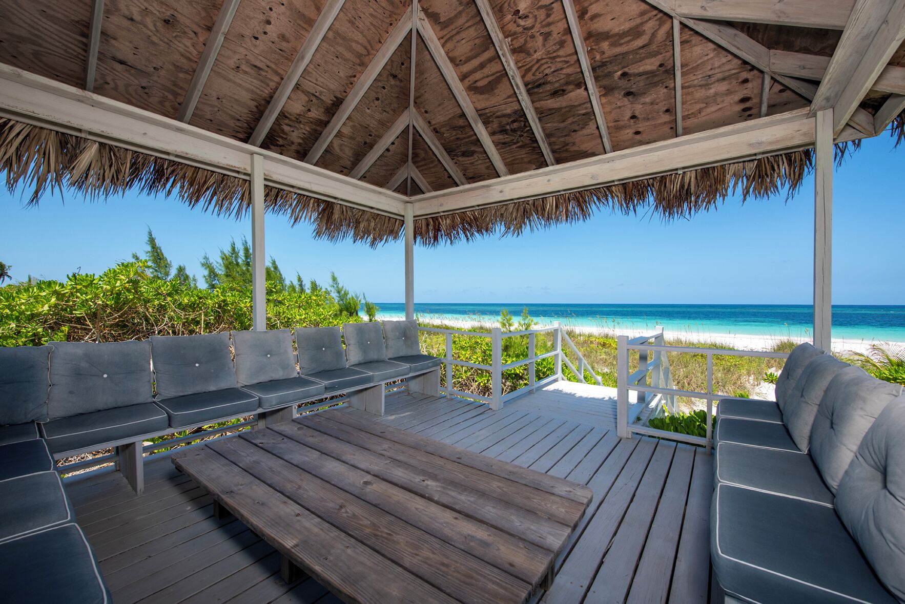 A wooden deck with benches and a table overlooking a beach.