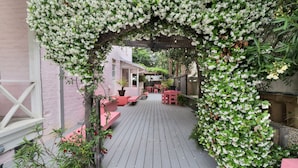 Une terrasse en bois avec une clôture rose et une pergola recouverte de fleurs blanches.