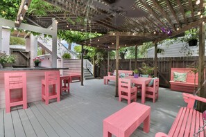 Eine überdachte Terrasse im Freien mit pinken Möbeln, einem Holzboden und einer Pergola mit Lichterketten.