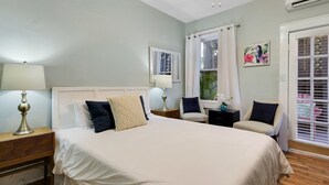 Une chambre à coucher avec un grand lit, deux tables de chevet, une chaise, une fenêtre avec des rideaux et une porte avec des stores.