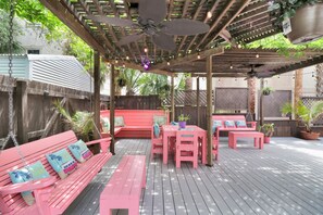 Eine Terrasse im Freien mit Holzboden, rosa Möbeln, Deckenventilatoren und Topfpflanzen.
