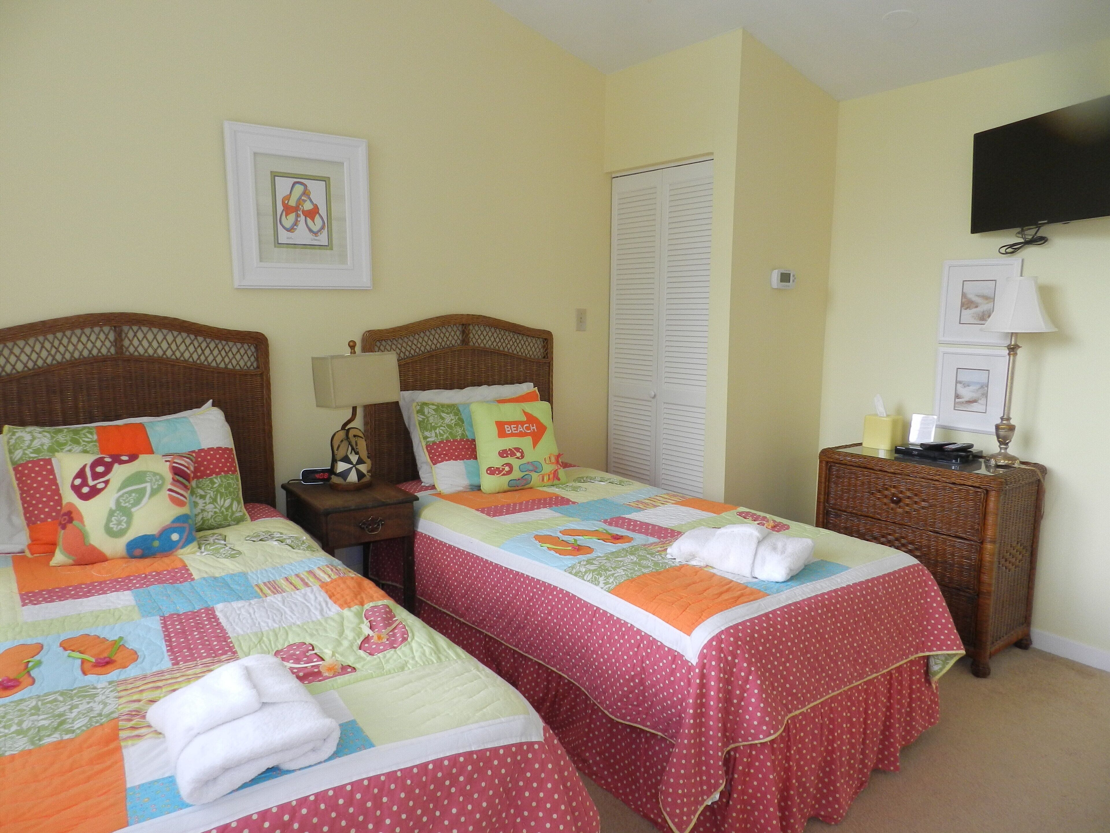 A bedroom with two beds, a nightstand, a lamp, a TV, and a window with blinds.