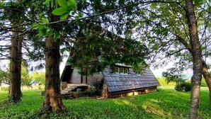 A rustic cabin with a sloped roof, surrounded by lush greenery and trees.
