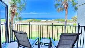 Ein Balkon mit zwei Stühlen und einem kleinen Tisch, mit Blick auf einen Strand mit Palmen und das Meer.
