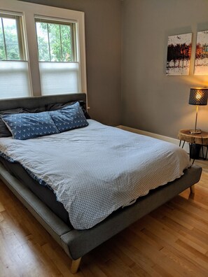 A bedroom with a bed, a nightstand, a lamp, and two windows.