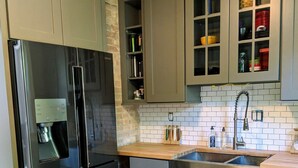 Una cocina moderna con gabinetes grises, un refrigerador de acero inoxidable, una encimera de madera y un lavamanos con grifo.