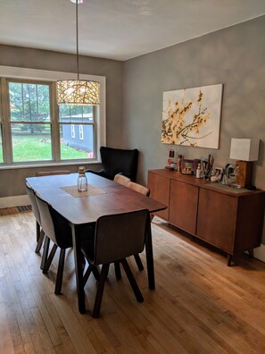 A dining area with a wooden table and chairs, a dark leather chair, a wooden cabinet with various items, and a large window with a view of the outdoors.