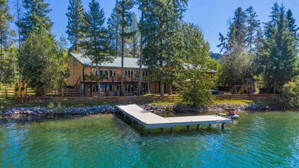 A lakeside property with a dock extending into the water, surrounded by tall trees. - Amazing Flathead River Location Gunner River Lodge (Bigfork)