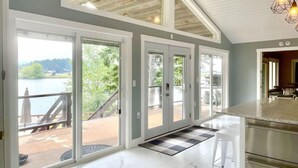 A spacious kitchen with a large island, a sliding glass door leading to a deck, and a view of a lake. - Amazing Flathead River Location Gunner River Lodge (Bigfork)