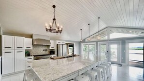 A spacious kitchen with a large island, white cabinetry, and a modern chandelier. - Amazing Flathead River Location Gunner River Lodge (Bigfork)