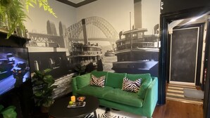 Ein Wohnzimmer mit einem grünen Sofa, einem Zebra-Teppich und einem Wandgemälde einer Brücke.