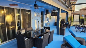Eine Terrasse im Freien mit Korbmöbeln, einem Glastisch und Deckenventilatoren.