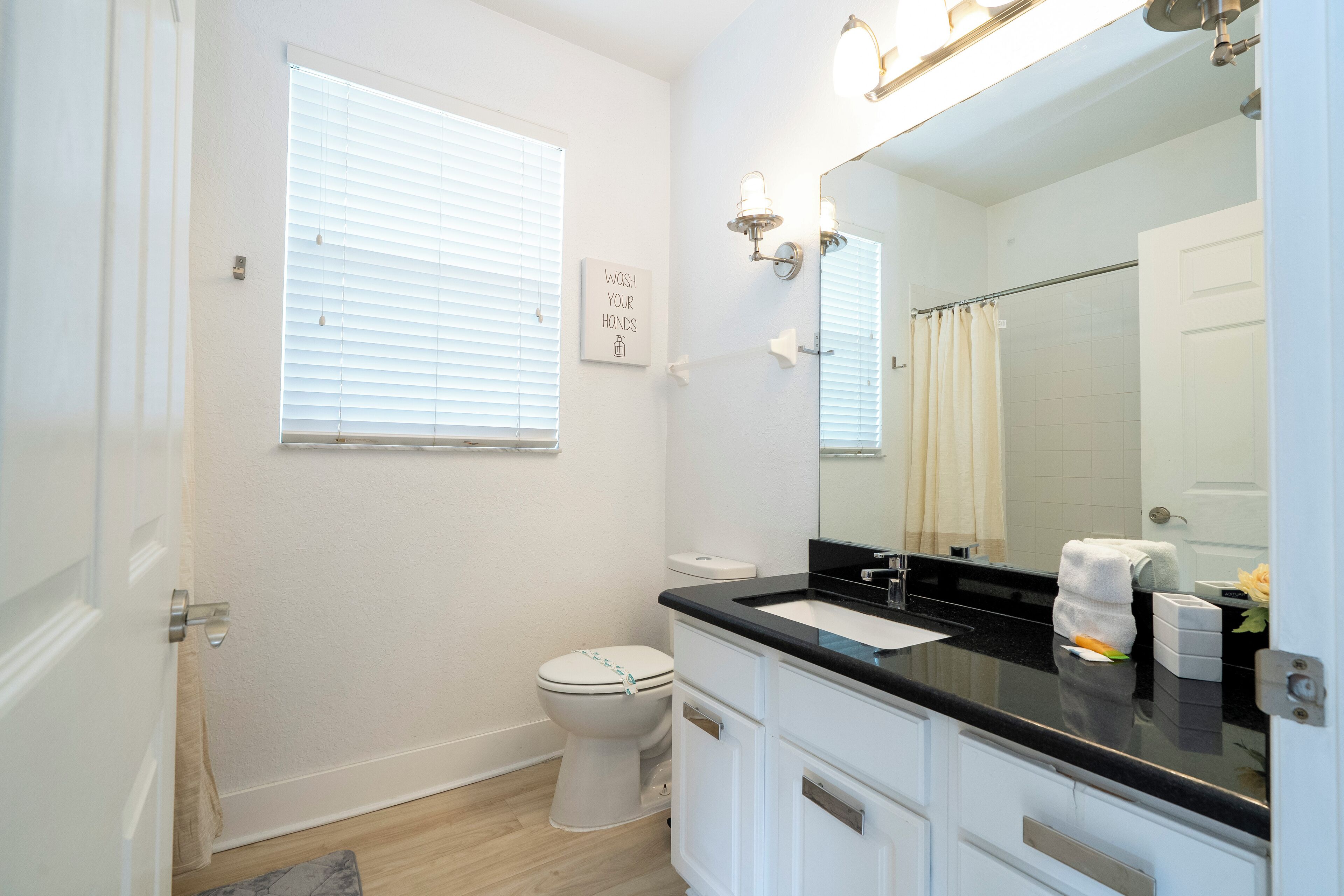 A bathroom with a toilet, sink, mirror, and window.