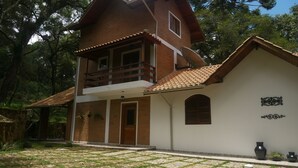 A two-story house with a balcony, a front door, and a small garden area with potted plants. - BEAUTIFUL HOUSE 5 MINUTES FROM THE CENTER – MONTE VERDE (Monte Verde)