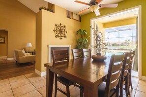A dining area with a wooden table and chairs, a ceiling fan, and a view of a swimming pool through a glass door.