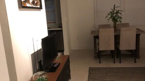 A dining area with a table and chairs, a television on a stand, and a plant on the table. - Beautiful updated apartment in a great location (Miami)