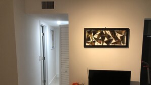 A hallway with a door leading to another room, a wall-mounted decorative panel, and a television on a wooden stand. - Beautiful updated apartment in a great location (Miami)
