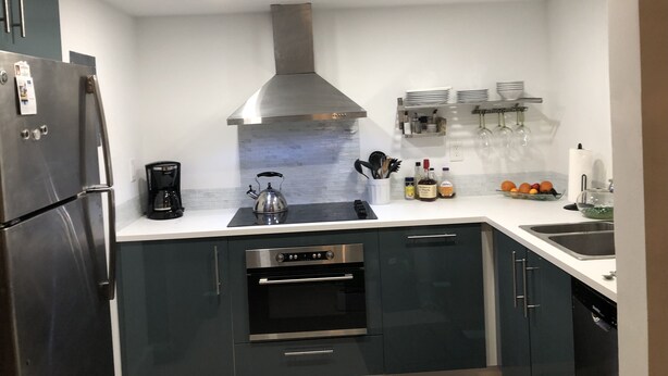 A modern kitchen with dark cabinets, a stainless steel range hood, a built-in oven, and a coffee maker. - Beautiful updated apartment in a great location (Miami)