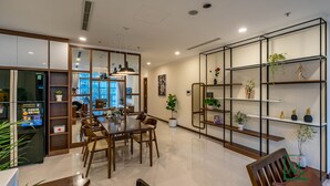 A modern kitchen with a dining area, featuring a refrigerator, wooden cabinets, and a dining table with chairs. - AMAVI LUXURY - VINHOMES SPACIOUS AND COZY APT FOR FAMILY/GROUP - 4 BR  (Ho Chi Minh)