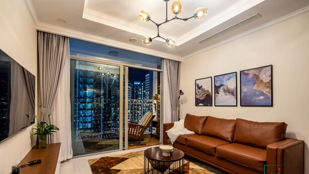 A modern living room with a brown leather sofa, a round coffee table, and a city view through large windows. - AMAVI LUXURY - VINHOMES SPACIOUS AND COZY APT FOR FAMILY/GROUP - 4 BR  (Ho Chi Minh)
