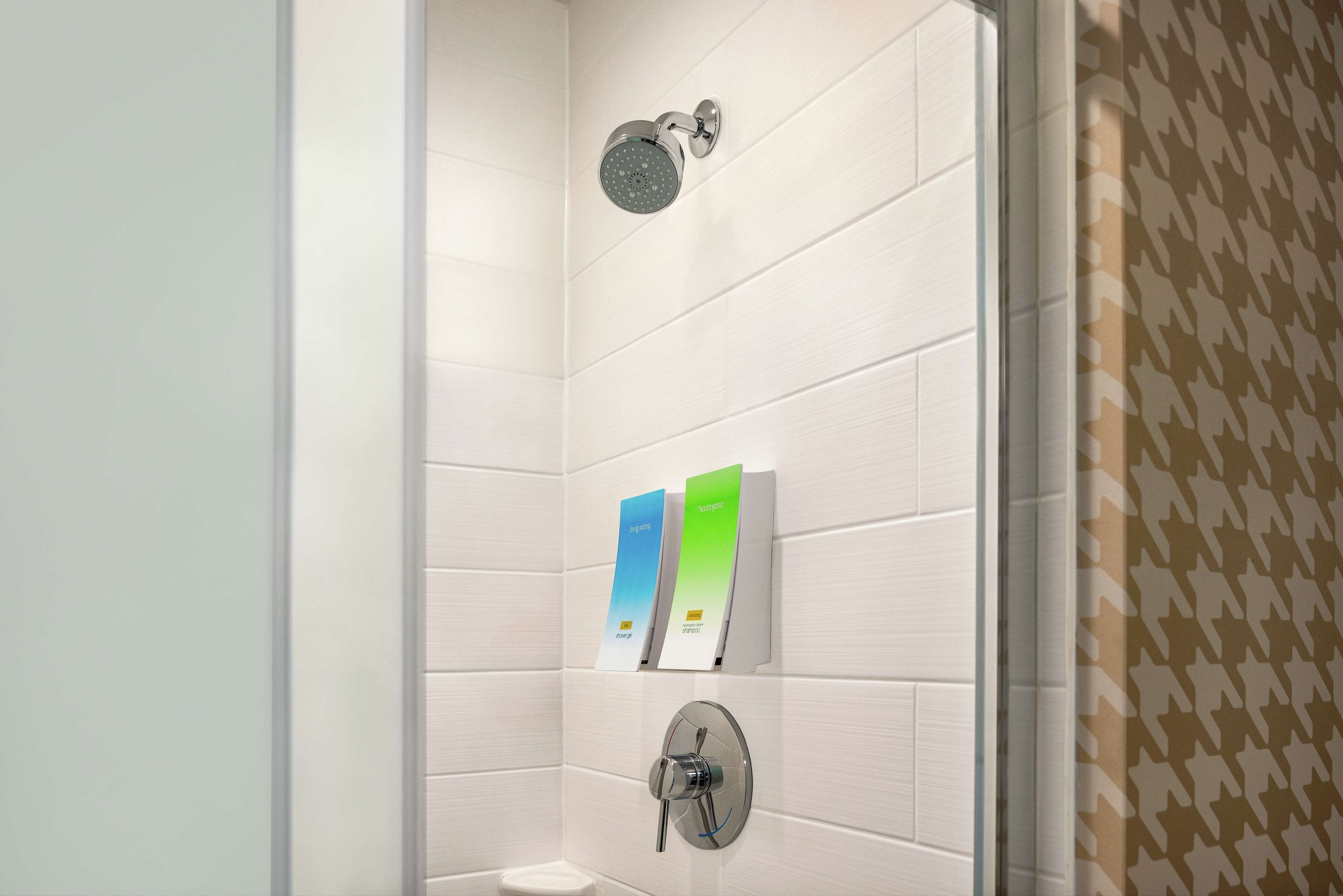 A shower with a handheld showerhead and a wall-mounted control valve. There are two informational cards on the wall.