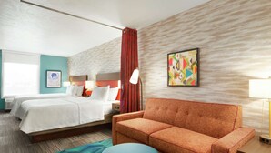 Habitación de hotel con cama, sofá, otoman redonda, lámpara y un cuadro en la pared.