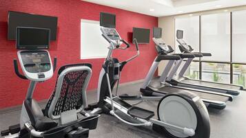 Un gimnasio con cintas de correr, una elíptica y una bicicleta estática, todo con pantallas digitales.