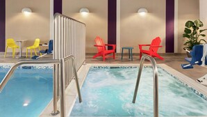 Una piscina interior con una escalera de metal, sillas amarillas y rojas, y una planta en maceta.