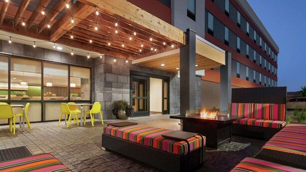 Un patio al aire libre con mobiliario de mimbre, una chimenea y luces colgantes.