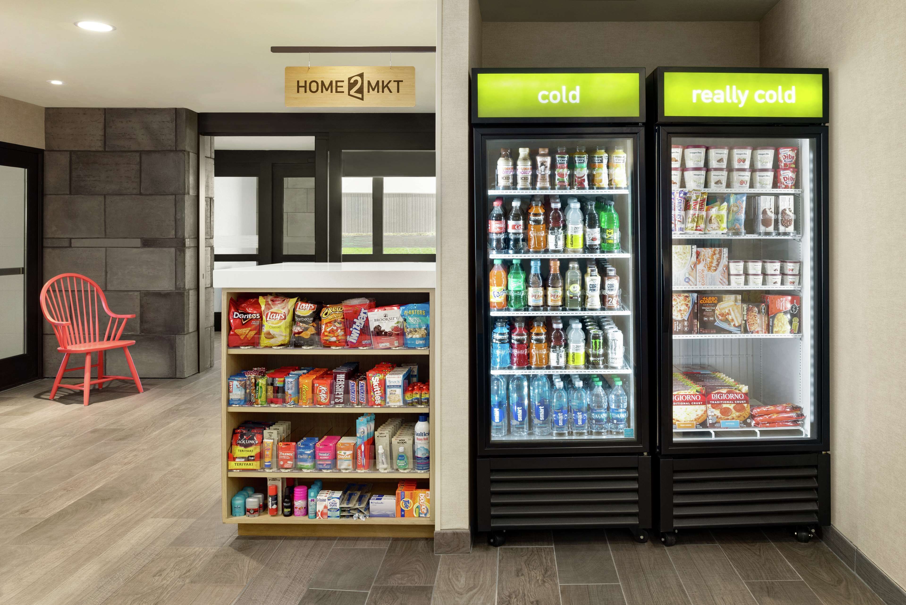 Un espace avec des distributeurs automatiques proposant des collations et des boissons, un panneau indiquant « HOME MKT », et une chaise rouge.