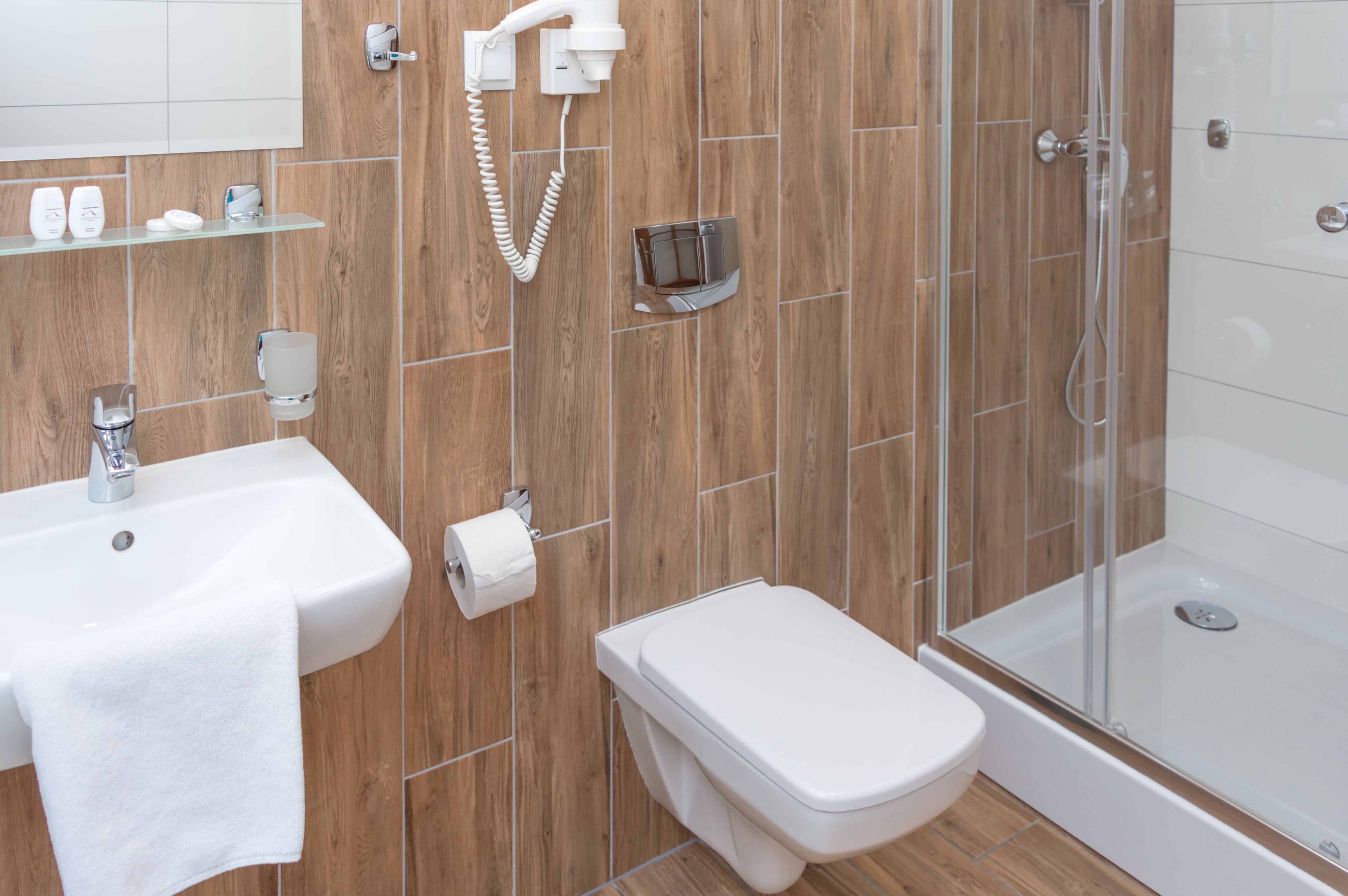 A modern bathroom with a wooden wall, a white sink, a toilet, and a glass-enclosed shower.