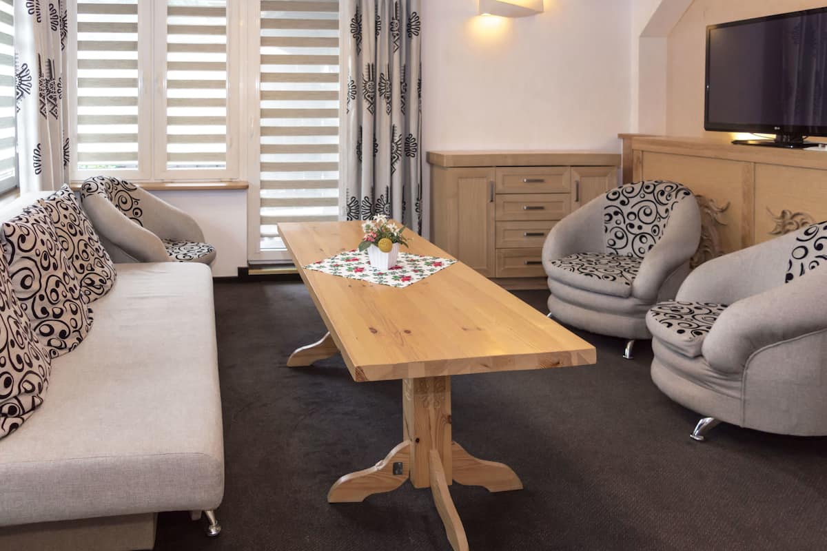 A living room with a sofa, two armchairs, a wooden coffee table, a television, and a cabinet.