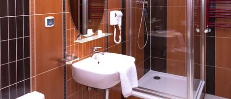 A bathroom with a white sink, a mirror, a handheld hair dryer, and a glass-enclosed shower.