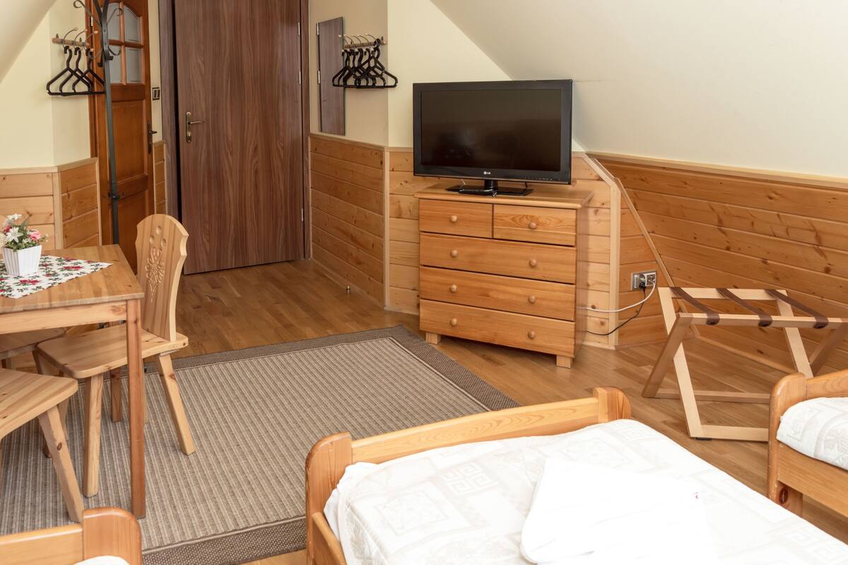 A room with a wooden dresser, a television, a bed, and a dining table with chairs.