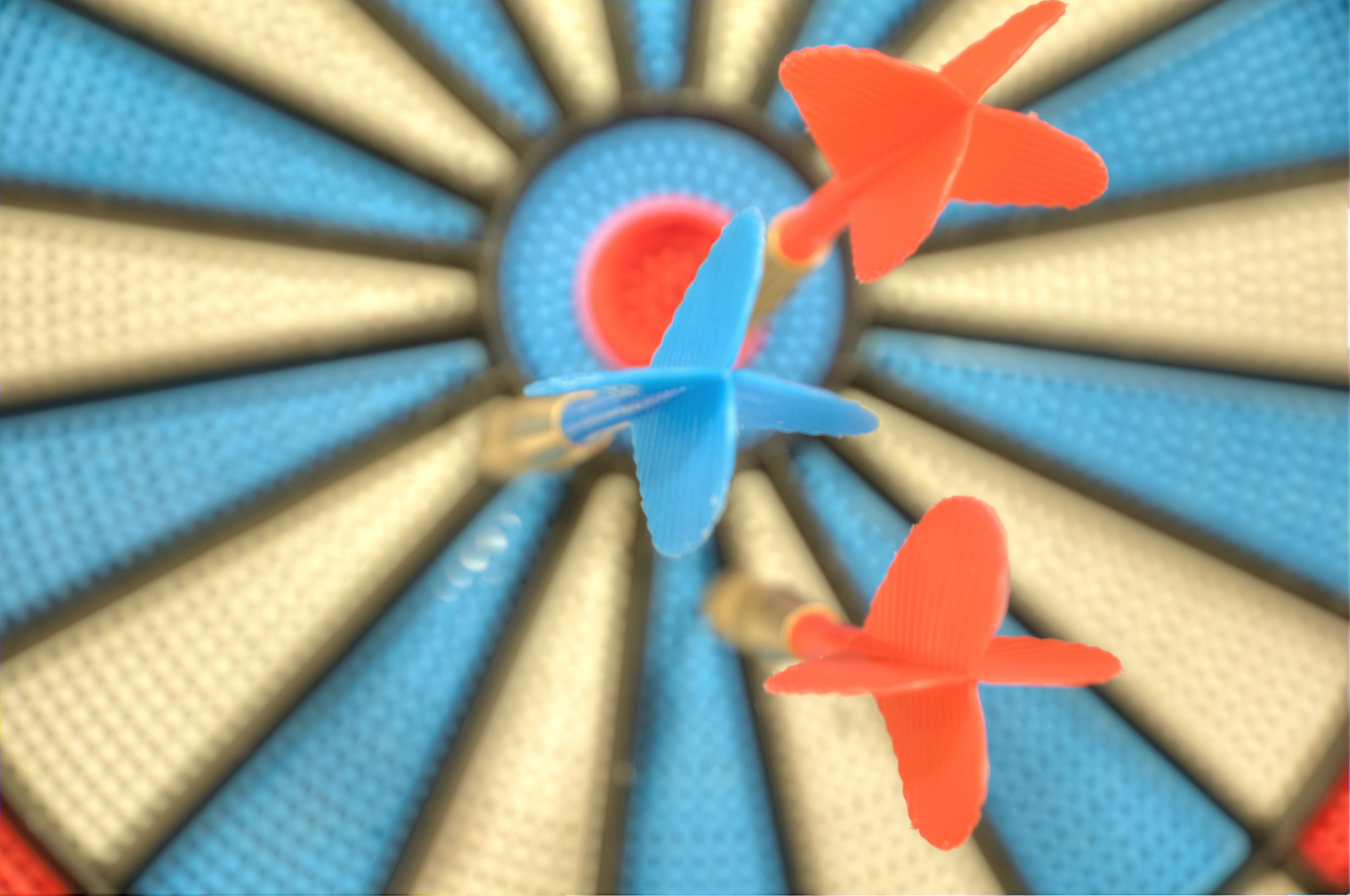 Eine Dartscheibe mit einer Zielscheibe in der Mitte und drei Dartpfeilen in Blau und Rot.
