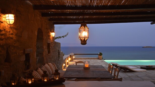 An outdoor dining area with stone walls, a view of the sea, and hanging lanterns. -  Villa With Swimming Pool In Front Of Almost Private Beach  (PAROS)