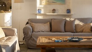 A cozy living room with a beige sofa, a wooden coffee table, and a painting of a beach scene on the wall. -  Villa With Swimming Pool In Front Of Almost Private Beach  (PAROS)