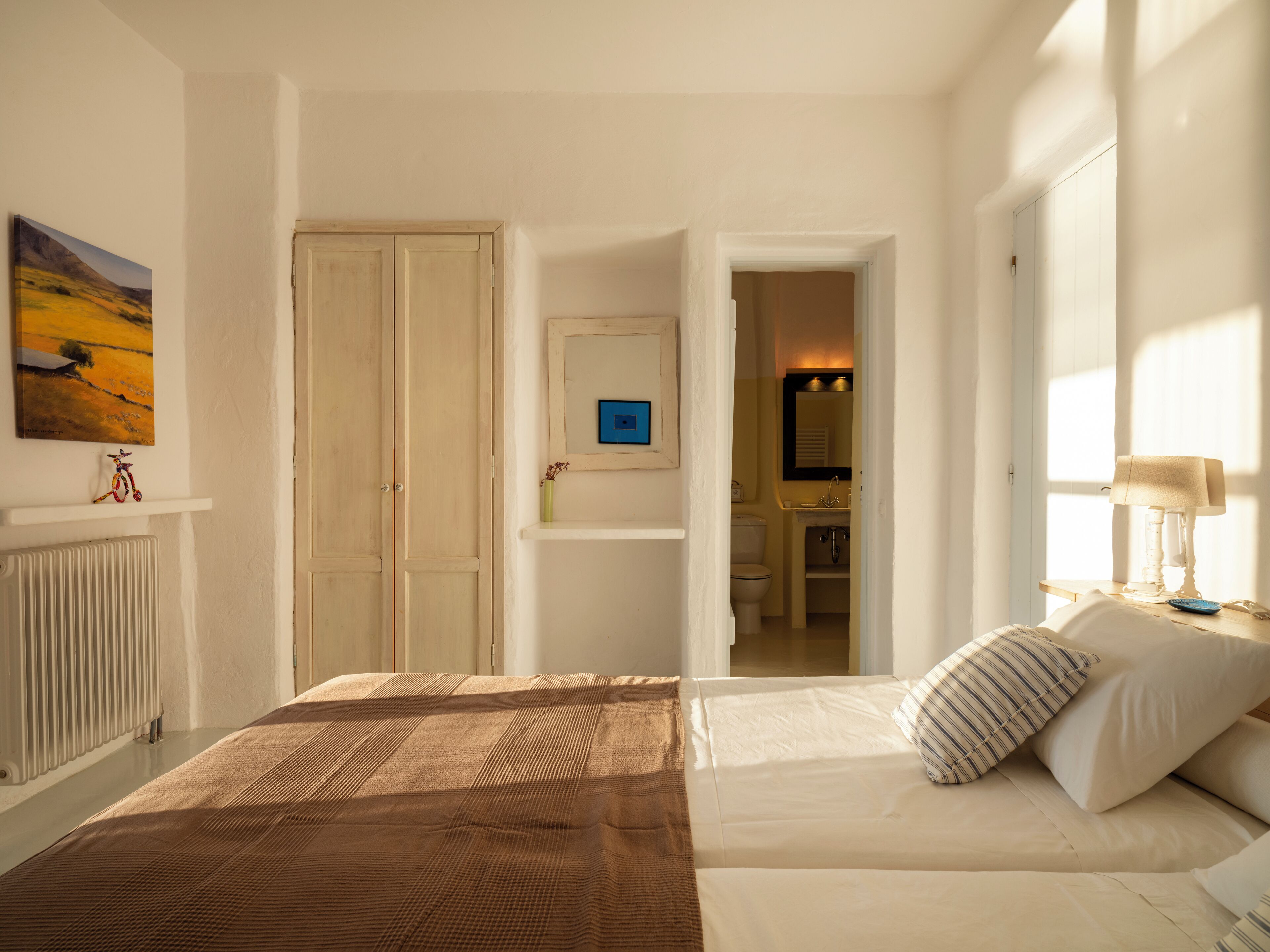 Ein Schlafzimmer mit Bett, Nachttisch, Lampe und Blick auf ein Badezimmer.