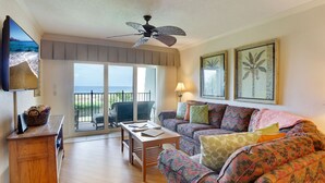 A living room with a sofa, a coffee table, a TV, and a balcony with a view of the ocean. - Land's End 304 bldg 7~Gated Community, Updated (Treasure Island)