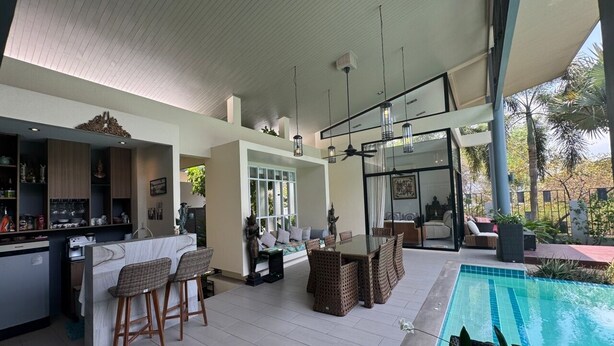 A modern outdoor kitchen with bar stools, a dining area with a table and chairs, and a pool.