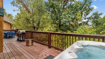 Una terraza de madera con jacuzzi, parrilla y mobiliario exterior.