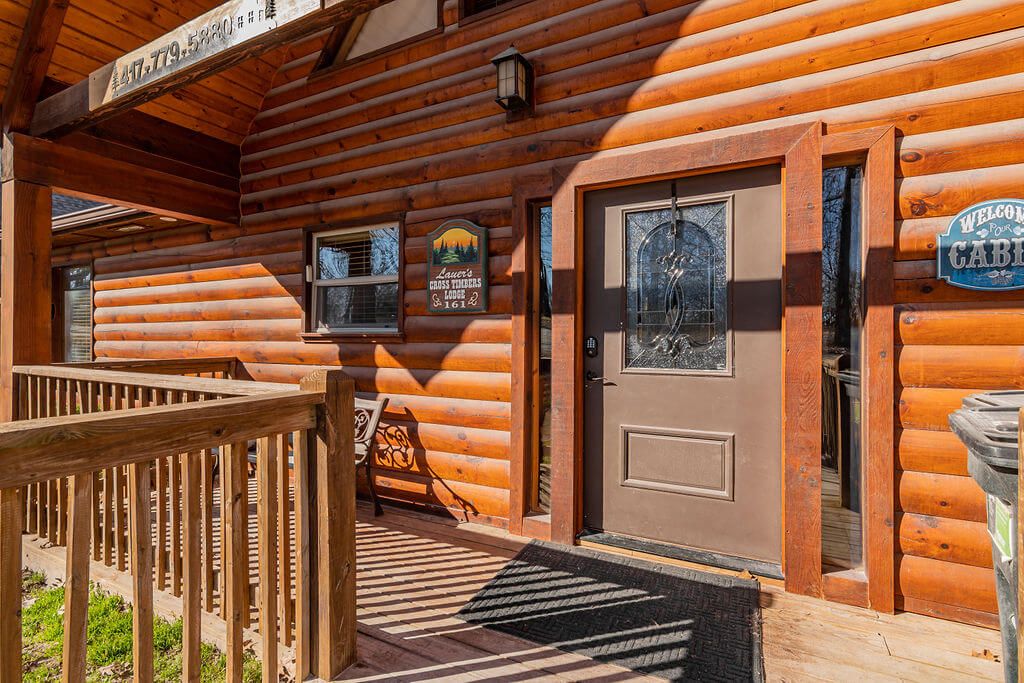 A wooden log cabin with a front door, a bench, and a welcome sign.